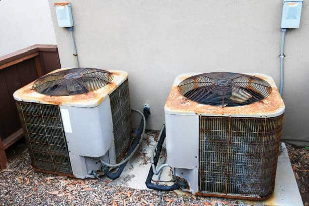Rusty air conditioner outdoor units set next to backyard facing house wall
